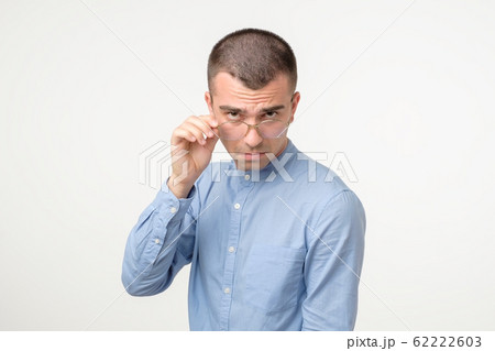 Doubtful young hispanic man looking with disbelief expression through glasses. 62222603