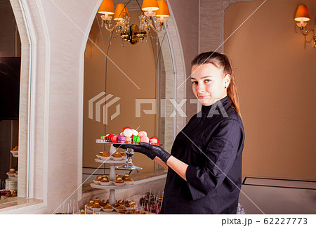 The waiter serves a stand of colorful macaroons at sweet table. 62227773