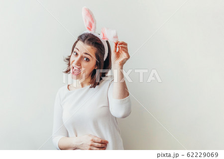 Happy Easter holiday celebration spring concept. Young woman wearing bunny ears isolated on white background. Preparation for holiday. Girl looking happy and excited having fun on Easter day Happy Easter holiday celebration spring concept. Young woman wearing bunny ears isolated on white background. Preparation for holiday. Girl looking happy and excited having fun on Easter day 62229069