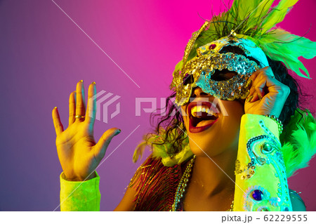 Beautiful young woman in carnival and masquerade costume on gradient studio background in neon light 62229555