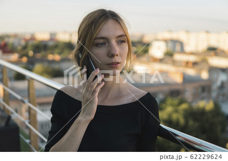 Young business woman using smart mobile phone, outside office building and speaking with a business partners. Business lady answering the phone with a smile, receiving good news. Freelancer. 62229624