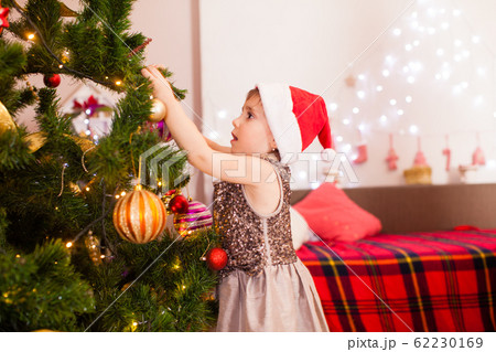Happy child girl decorating Christmas tree at home 62230169