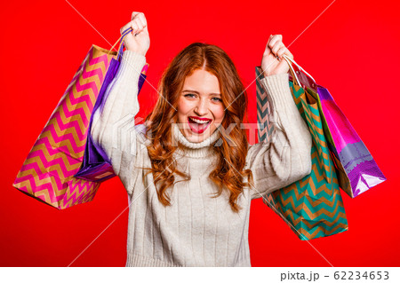 Happy young woman with red hair and paper bags after shopping isolated on studio background. Seasonal winter sale, purchases, spending money on gifts concept 62234653