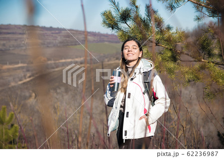 woman hiking a hill stopped for a drink. woman traveler drinking tea from a thermos on hill 62236987
