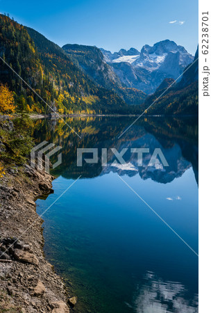 Peaceful autumn Alps mountain lake with clear transparent water and reflections. Gosauseen or Vorderer Gosausee lake, Upper Austria. Dachstein summit and glacier in far. 62238701