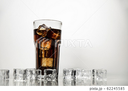 A refreshing drink of stake is poured into a glass beaker. Cola on white background with scattered ice cubes. A refreshing drink of stake is poured into a glass beaker. Cola on white background with scattered ice cubes. 62245585