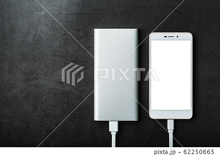 A white Powerbank charges a smartphone on a black 62250665