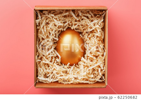 Golden egg in a box with shavings on a pink Golden egg in a box with shavings on a pink 62250682