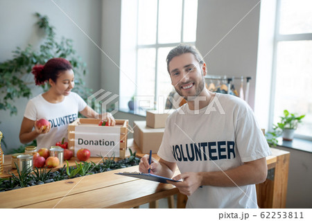 Young man with folder, girl putting fruits in a box. Young man with folder, girl putting fruits in a box. 62253811