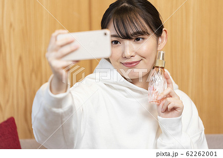 化粧品のボトルを持ってスマホでセルフィーを撮る若い女性 インスタグラマー インフルエンサー イメージの写真素材