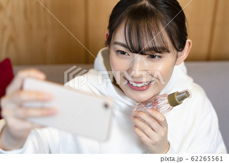 化粧品のボトルを持ってスマホでセルフィーを撮る若い女性 インスタグラマー インフルエンサー イメージの写真素材