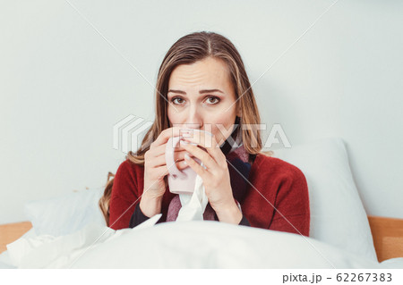 Woman with hot tea and the flu lying in bed sick Woman with hot tea and the flu lying in bed sick 62267383