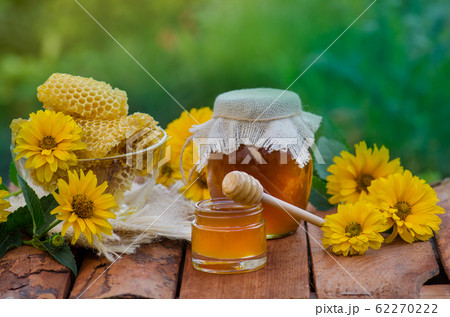 Honey jar and wooden stick on table against green Honey jar and wooden stick on table against green 62270222