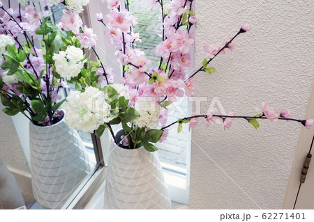 Bright pink and white colored fake flowers in a white vase near a window on a light day, plastic flowers in modern room 62271401