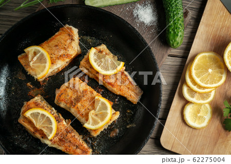 Portioned pieces of fried fish in a black cast-iron pan with fresh cucumbers and herbs. Traditional dinner of a village fisherman, top view, flat lay 62275004