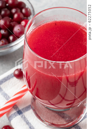One glass with homemade freshly cranberry juice and a bowl of cranberries on a gray concrete table, vertical image One glass with homemade freshly cranberry juice and a bowl of cranberries on a gray concrete table, vertical image 62275052