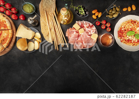 Italian food with a place for text, a flat lay design template for a restaurant. Pizza, pasta, cheese, ham, wine, olives, pesto, capers, olive oil, tomatoes, shot from the top 62282187