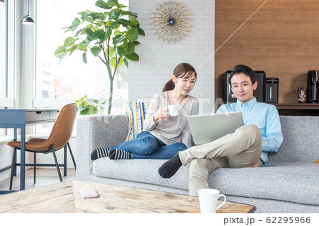 リビングルームでパソコンを覗き込みながら話をする若いカップル 62295966