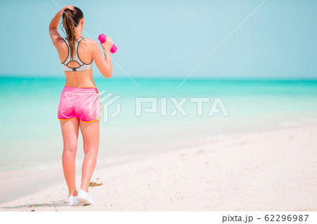 Fit young woman doing exercises on tropical white beach in her sportswear Fit young woman doing exercises on tropical white beach in her sportswear 62296987