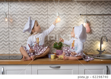 Two sisters sit on the kitchen table and drink tea  62298740