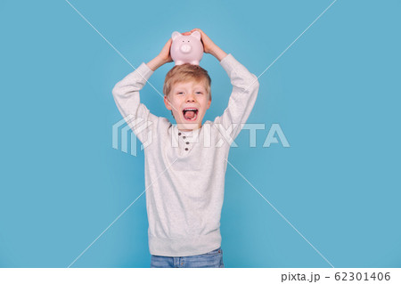 Excited little boy with piggy bank on blue background Excited little boy with piggy bank on blue background 62301406