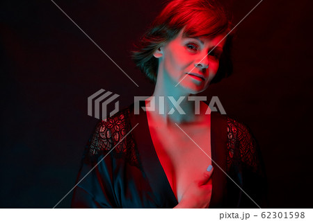 Beautiful attractive woman posing in satin bathrobe in neon light. 62301598