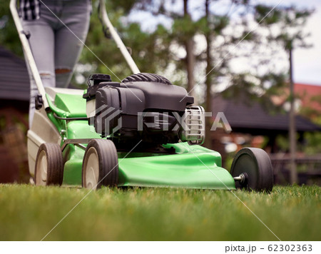 Female legs of girl using lawn mower. 62302363