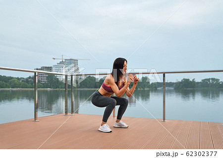 Young fitness girl exercising on pier during morning workout 62302377