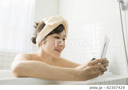 バスルームで防水ケースにスマホを入れて操作する若い女性 62307429