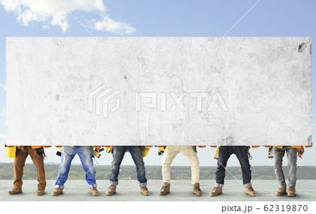 Builders with tools in construction clothing hold a heavy slab Builders with tools in construction clothing hold a heavy slab 62319870
