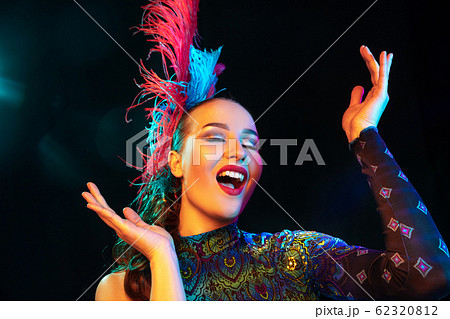 Beautiful young woman in carnival and masquerade costume in colorful neon lights on black background Beautiful young woman in carnival and masquerade costume in colorful neon lights on black background 62320812