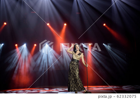 Singer in a dress on stage in the rays of bright light with smoke. 62332075