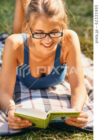 young, beautiful girl holding an open book, read background summer green park 62335995