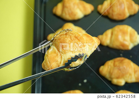 焼きたてパン　トングでパンをとるイメージ。パン屋や手作りパンのイメージ　黄色背景 62342558