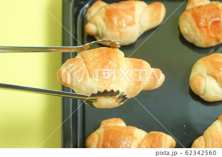 焼きたてパン　トングでパンをとるイメージ。パン屋や手作りパンのイメージ　黄色背景 62342560