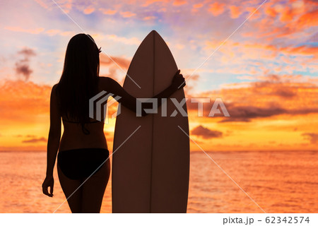 Beach sunset sexy surfer woman surfing lifestyle relaxing holding surfboard looking at ocean waves for surf. Active healthy living silhouette of sports athlete standing in colorful sky Beach sunset sexy surfer woman surfing lifestyle relaxing holding surfboard looking at ocean waves for surf. Active healthy living silhouette of sports athlete standing in colorful sky 62342574
