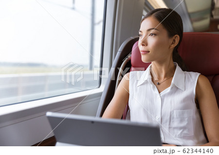 Asian woman traveling using laptop in train. Businesswoman pensive looking out the window while working on computer on travel commute to work Asian woman traveling using laptop in train. Businesswoman pensive looking out the window while working on computer on travel commute to work 62344140