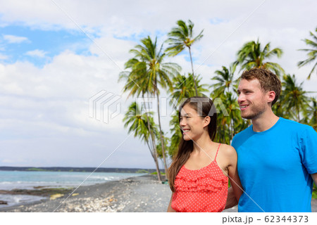 Interracial couple on Hawaii holiday enjoying view of ocean from black sand volcanic beach on Big Island of Hawaii, hawaiian vacation destination 62344373