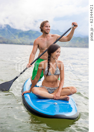 Paddleboard couple having fun paddleboarding together on Hawaii beach vacation summer holidays. Woman sitting on board while man paddles 62344421