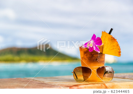 Hawaii mai tai cocktail drink on waikiki beach bar with flower, pineapple and sunglasses. View of the ocean and diamond head mountain in Honolulu, Hawaii. Summer vacation Hawaii mai tai cocktail drink on waikiki beach bar with flower, pineapple and sunglasses. View of the ocean and diamond head mountain in Honolulu, Hawaii. Summer vacation 62344465
