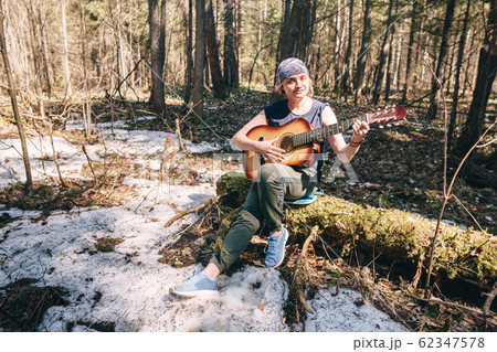Young woman playing guitar sitting on old tree covered with moss at sunny spring forest Young woman playing guitar sitting on old tree covered with moss at sunny spring forest 62347578