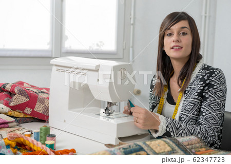 Cheerful young seamstress with her sewing machine Cheerful young seamstress with her sewing machine 62347723