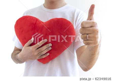 ハートのクッションを持ってサムズアップしている白いシャツを着た男性 ハートのクッションを持ってサムズアップしている白いシャツを着た男性 62349016