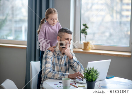 Seated focused dad, daughter standing behind, they are looking into laptop. 62351847