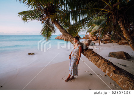 La Digue, Seychelles. A woman near coconut palm tree in a gold sunset light on a tropical beautiful sandy beach 62357138