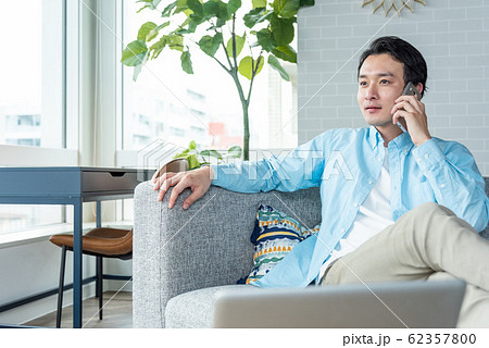自宅 リビングルームでスマホを片手に話をする若い男性 自宅 リビングルームでスマホを片手に話をする若い男性 62357800