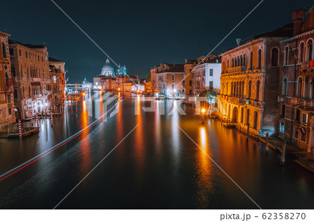 Venice, Italy night scenery of Grand Canal. Vivid light trails of ferries and boats reflected on water surface. Majestic Basilica di Santa Maria della Salute in background 62358270