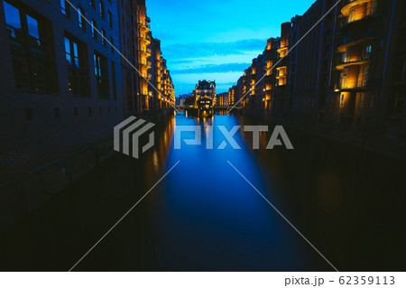 Wide perspective of Warehouse District - Speicherstadt in twilight. Blue hour. Tourism landmark of Hamburg. View of Wandrahmsfleet in light of lantern lamp in HafenCity Wide perspective of Warehouse District - Speicherstadt in twilight. Blue hour. Tourism landmark of Hamburg. View of Wandrahmsfleet in light of lantern lamp in HafenCity 62359113