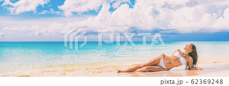 Beach paradise sexy bikini woman lying down on sand relaxing sun tanning in tropical caribbean travel destination for summer vacation. Panoramic banner landscape with copy space on blue ocean Beach paradise sexy bikini woman lying down on sand relaxing sun tanning in tropical caribbean travel destination for summer vacation. Panoramic banner landscape with copy space on blue ocean 62369248