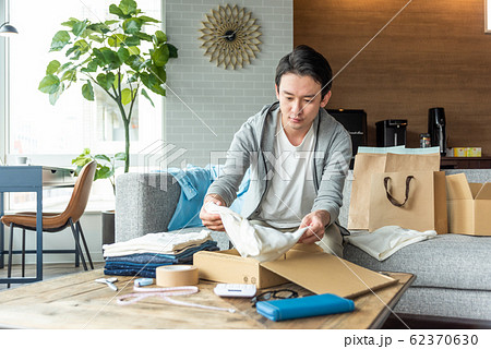 メルカリにいらない服を出そうと箱詰めしている若い男性 62370630